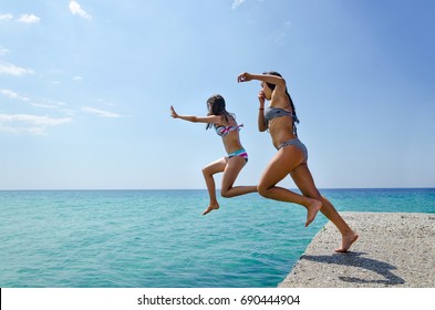 Kids Jumping Off The Dock Into A Turguise Sea Water. Having Fun On A Summer Vacation With Friends