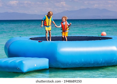 Kids Jumping On Trampoline On Tropical Sea Beach. Children Jump On Inflatable Water Slide. Aqua Amusement Park In Exotic Island Resort. Family Vacation And Travel With Child. Ocean Coast Fun.