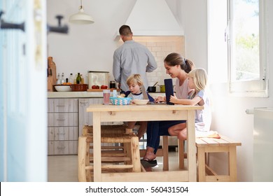 Kids At Kitchen Table With Mum, Dad Cooks, View From Doorway