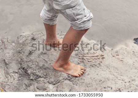 Kid's lags with river mud. Fun childhood game. Research nature. Happy young boy in mud playing outside in the river on a summer day.