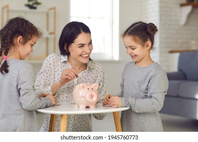 Kids Learn To Handle Money. Mom Teaches Her Two Little Daughters Financial Literacy And Puts Money In A Piggy Bank For Future Investments. Concept Of Teaching Children Budget Management And Savings.