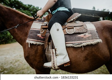 Kids Learn To Ride A Horse.Happy Asian Kid Girl Riding Horse In Horse School Farm Club With Leather Boots Horseback Riding, Lovely Powerful Equestrian.Cowgirl Kid Fun In Farm.