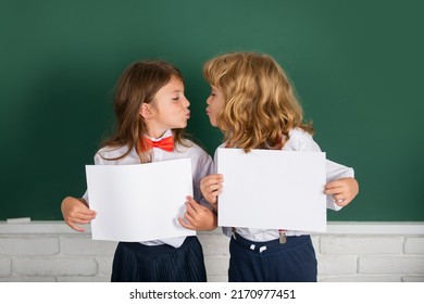 Kids love, first kiss. Back to school. Schoolchild friends back to school at knowledge day. Schoolkids holding white paper blank, poster with copy space.