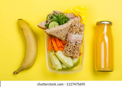 Kids Lunch Box With Sandwich, Vegetable Sticks, Granola Bar, Banana And Juice On Yellow Background. Back To School Concept