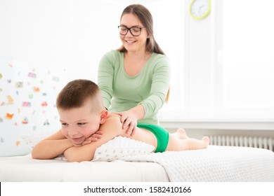 Kids Massage Concept Background. Young Female Massage Therapist Giving A 6 Year Old Boy Back Massage. Physical Therapy.