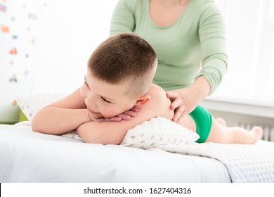 Kids Massage Concept Background. Young Female Massage Therapist Giving A 6 Year Old Boy Back Massage. Physical Therapy.