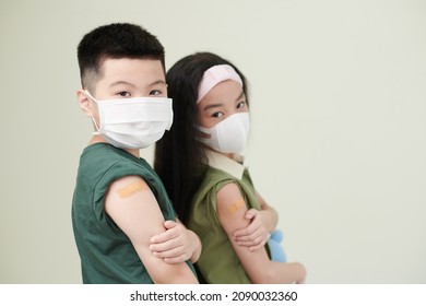 Kids in medical masks showing shoulder with adhesive plasters after they got vaccinated against coronavirus