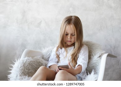 Kids, Modern Technology And Addiction. Portrait Of Concentrated Female Child With Loose Straight Hair Typing Text Message To Her Cousin Using Wireless Internet Connection On Mother's Mobile Phone