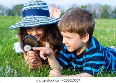 Kids On The Meadow Looking To Dandelion With A Magnifying Glass