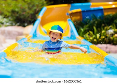 Kids On Water Slide In Aqua Park. Children Having Fun On Water Slides On Family Summer Vacation In Tropical Resort. Amusement Park With Wet Playground For Young Child And Baby.