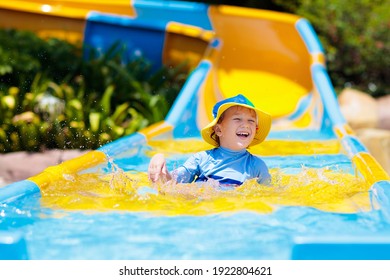 Kids On Water Slide In Aqua Park. Children Having Fun On Water Slides On Family Summer Vacation In Tropical Resort. Amusement Park With Wet Playground For Young Child And Baby.