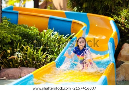 Kids on water slide in aqua park. Children having fun on water slides on family summer vacation in tropical resort. Amusement park with wet playground for young child and baby.