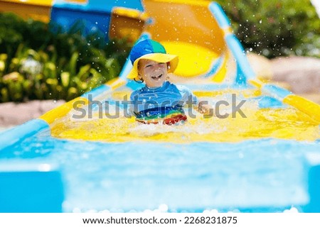Kids on water slide in aqua park. Children having fun on water slides on family summer vacation in tropical resort. Amusement park with wet playground for young child and baby.