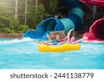 Kids on water slide in outdoor swimming pool. Family in aqua theme park. Children have fun in splash playground. Summer vacation with child. Kid on inflatable tube sliding into a pool.