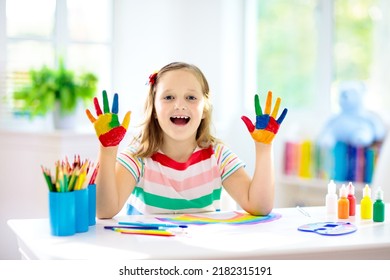 Kids paint. Child painting in white sunny study room. Little girl drawing rainbow. School kid doing art homework. Arts and crafts for kids. Paint on children hands. Creative little artist at work.