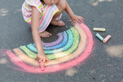   Дети рисуют на открытом воздухе. Портрет девочки, рисующей радужным цветным мелом на асфальте в летний солнечный день. Творческое развитие детей