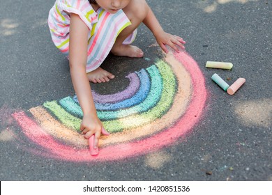   Kids paint outdoors. Portrait of a child girl drawing  a rainbow colored chalk on the asphalt on summer sunny day. Creative development of children - Powered by Shutterstock