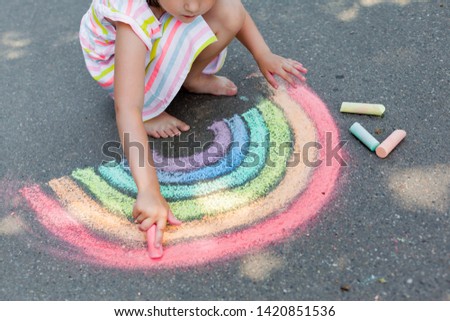   Kids paint outdoors. Portrait of a child girl drawing  a rainbow colored chalk on the asphalt on summer sunny day. Creative development of children