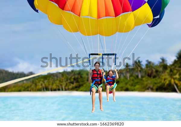 Kids\
parasailing. Water sport on summer vacation. Brother and sister\
flying in tropical ocean resort. Sea and beach fun. Rainbow\
parachute. Teenage boy and little girl\
fly.