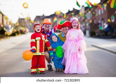 Kids And Parents On Halloween Trick Or Treat. Family In Halloween Costumes With Candy Bags Walking In Decorated Street Trick Or Treating. Baby And Preschooler Celebrating Carnival. Child Costume.