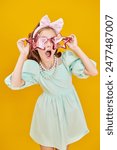 Kids party, holiday. Pretty emotional girl dresses up in bright fashionable outfits. Portrait on yellow studio background. Children