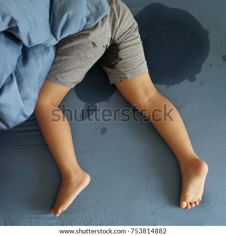 Kid's pee in a mattress. Little boy feet and pee in bed sheet. Child development concept.