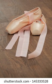 Kids Pink Ballet Shoes With Ribbons Lying On A Wooden Floor In The Ballet Hall