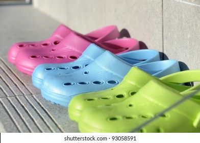 Kids Plastic Summer Clogs In A Row On A Step. Shot Through Glass. Shallow Depth Of Field. Focus On The Blue Clog.