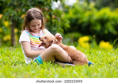 Kids Play With Cute Little Puppy. Children And Baby Dogs Playing In Sunny Summer Garden. Little Girl Holding Puppies. Child With Pet Dog. Family And Pets On Park Lawn. Kid And Animals Friendship.