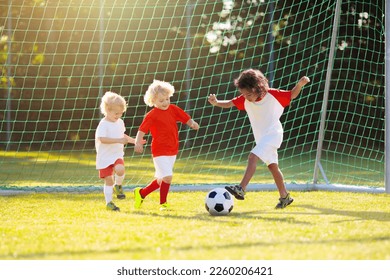 Kids play football. Cute little boy playing football. Children run on outdoor pitch. Sports class. Interracial group of kids play ball outdoor. Summer fun. Toddler running. Sport for active child.  - Powered by Shutterstock