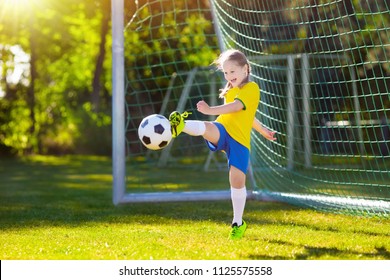 Kids play football on outdoor field. Brazil team fans. Children score a goal at soccer game. Little girl in Brazilian jersey and cleats kicking ball. Football pitch. Sports training for player.
