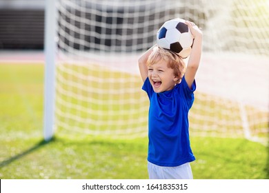 Kids Play Football On Outdoor Stadium Field. Children Score A Goal During Soccer Game. Little Boy Kicking Ball. School Sports Club. Training For Young Player.