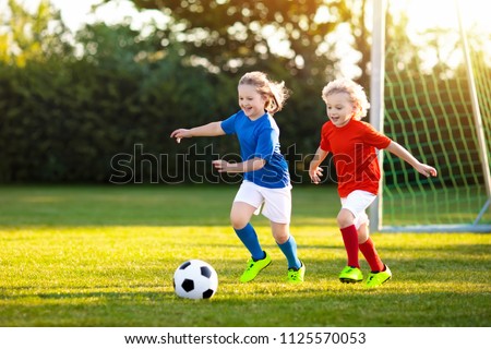 Kids play football on outdoor field. Children score a goal at soccer game. Girl and boy kicking ball. Running child in team jersey and cleats. School football club. Sports training for young player.