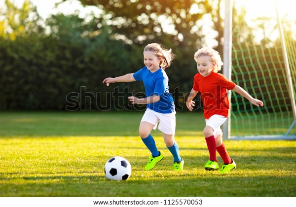 子供たちは野外でフットボールをする 子どもたちはサッカーの 試合でゴールを決める ボールを蹴る少女と少年 チームジャージーとクリートで子を実行しています 学校のサッカー部 若い選手のスポーツのトレーニング の写真素材 今すぐ編集