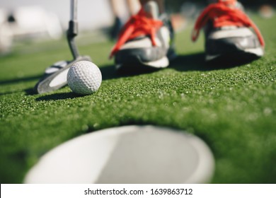Kids play mini golf. Close-up image of player in snickers with mini golf club and white golf ball. e cup in the foregroundGold hole th