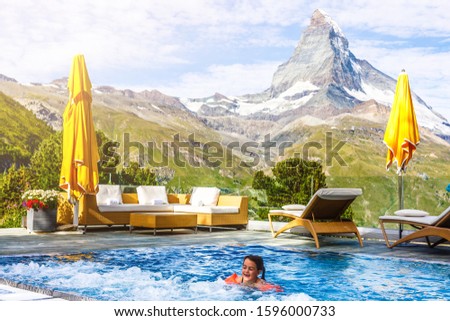 Kids play in outdoor infinity swimming pool of luxury spa alpine resort at sunset in Alps mountains. Spring or summer vacation for family with children.