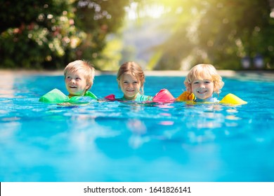 Kids Play In Outdoor Swimming Pool Of Tropical Resort. Swim Aid For Young Child. Baby Learning To Dive. Group Of Children Playing In Water. Colorful Life Jacket. Beach And Summer Fun.