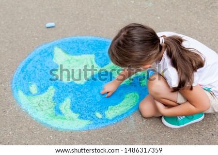Kids play outdoors. Child girl draws a planet globe with a map of the world colored chalk on the pavement, asphalt. Earth, peace day concept.