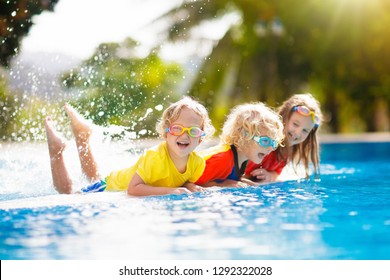 Kids Play In Swimming Pool. Children Learn To Swim In Outdoor Pool Of Tropical Resort During Family Summer Vacation. Water And Splash Fun For Young Kid On Holiday. Sun Protection For Child And Baby.