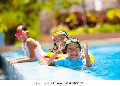 Kids play in swimming pool. Children learn to swim in outdoor pool of tropical resort during family summer vacation. Water and splash fun for young kid on holiday. Sun protection for child and baby. - Powered by Shutterstock