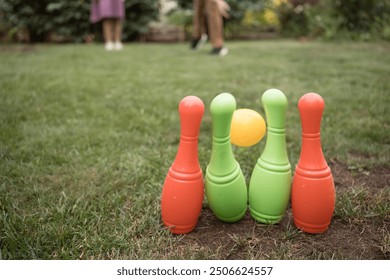 Kids play toy bowling with colorful plastic skittles and ball on grass in garden or yard or park in summer day - Powered by Shutterstock