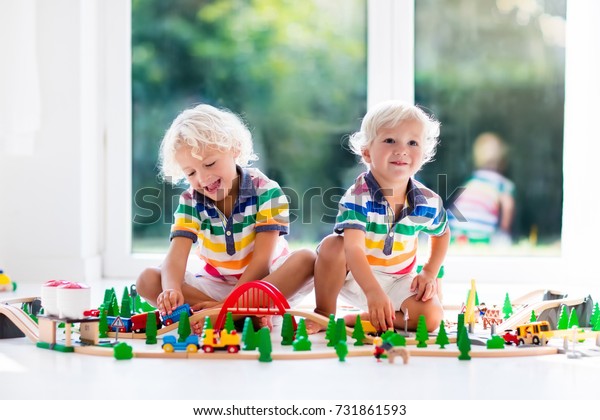 Kids play with toy train railway. Children playing\
with wooden trains. Toys for little boy. Two brothers build rail\
road and blocks at home or daycare, preschool. Kindergarten\
educational games.