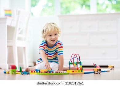 Kids play with wooden railway. Child with toy train. Educational toys for young children. Little boy building railroad tracks on white floor at home or kindergarten. Cute kid playing cars and engine.