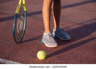Kids player tennis. Racquet and legs and ball. Summer activities for children in the tennis club. Cropped image of sports little girl on tennis court. Athletic child girl hits tennis ball with a racke