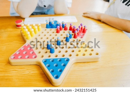 Kids are playing chinese checkers at a wooden table. Three-player gameboard of Diamond Game (variant of Chinese Checkers , variation of Halma strategy board game) on wooden table.