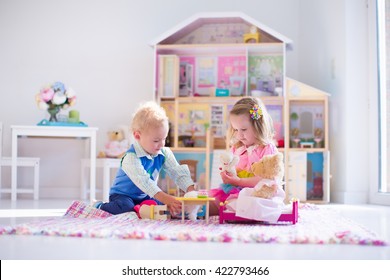 Kids playing with doll house and stuffed animal toys. Children sit on a pink rug in a play room at home or kindergarten. Toddler kid and baby with plush toy and dolls. Birthday party for little child.