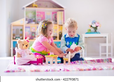 Kids playing with doll house and stuffed animal toys. Children sit on a pink rug in a play room at home or kindergarten. Toddler kid and baby with plush toy and dolls. Birthday party for little child.
