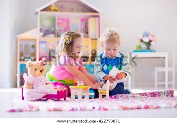 人形の家やぬいぐるみのおもちゃで遊ぶ子どもたち 子どもたちは家や幼稚園の遊び場でピンクの絨毯の上に座る プラシおもちゃと人形を持つ幼児と赤ちゃん 幼い子供の誕生日パーティー の写真素材 今すぐ編集