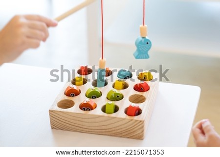 Kids are playing and finding the matched number in the wooden magnetic fishing game, using wooden fishing pole provided with magnets to attach the mouth of the fish and picking it up.