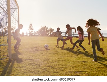 Kids playing football in a park, one in goal, side view